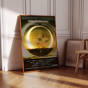 May include: A rectangular wall art print featuring the Breaking Benjamin album Dark Before Dawn. The design displays a solar eclipse graphic, a tracklist with song titles and durations, and the release date June 23, 2015, in a wooden frame.