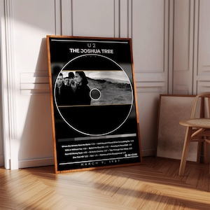 Może przedstawiać: Oprawiony plakat z albumem U2 "The Joshua Tree". Plakat ma czarne tło z okrągłym wzorem i czarno-białym zdjęciem zespołu. Widoczna jest również lista utworów z albumu oraz data 9 marca 1987.