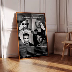 May include: A framed black and white poster featuring the band U2. The poster has the text "U2 SONGS OF SURRENDER" at the top and the band members' faces in a circular design. The date "MARCH 17, 2023" is at the bottom.