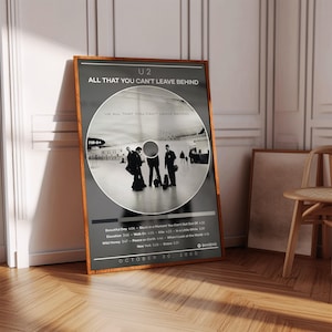Może przedstawiać: Oprawiony plakat z albumem U2 "All That You Can't Leave Behind". Plakat ma czarne tło z obrazem przypominającym płytę CD pośrodku. Wyświetlony jest tytuł albumu i lista utworów. Rama jest w ciepłym brązowym kolorze.