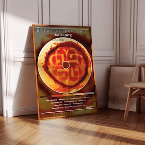 May include: A rectangular poster featuring the Breaking Benjamin album Saturate. The design includes a central circular graphic with red and yellow tones, a tracklist with song titles and durations, and the release date August 27, 2002.