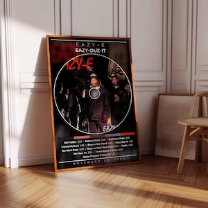 Puede incluir: Un póster enmarcado con la portada del álbum "Eazy-Duz-It" de Eazy-E. La obra de arte incluye una imagen circular de Eazy-E y otras figuras. El póster tiene un fondo negro con texto blanco, incluyendo títulos de canciones y la fecha 23 de noviembre de 1988.
