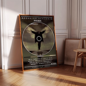 May include: A rectangular framed poster featuring the Breaking Benjamin album Phobia. The design includes a central circular image of a figure with wings, the text Breaking Benjamin Phobia, a tracklist, and the release date August 8, 2006.