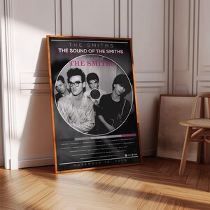 Peut inclure: A framed poster of the band The Smiths, with the text "THE SMITHS THE SOUND OF THE SMITHS." The poster has a black background with a circular image of the band. The date "NOVEMBER 10, 2008" is printed at the bottom.