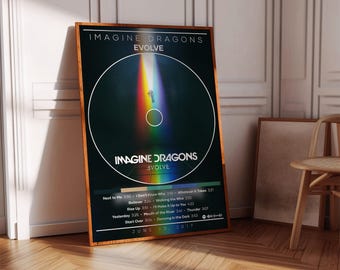 Puede incluir: Un póster enmarcado del álbum "Evolve" de Imagine Dragons. El póster tiene un fondo negro con un diseño circular y un haz de luz de arcoíris. El título del álbum y la lista de canciones son visibles. La fecha "25 de junio de 2017" está impresa en la parte inferior.