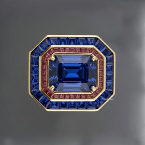 Pode incluir: Um anel dourado com uma grande pedra preciosa retangular azul escura no centro, rodeada por pedras preciosas azuis e rosas menores. O anel tem formato octogonal e uma aparência luxuosa.
