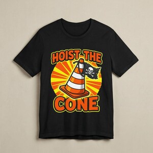 Puede incluir: Camiseta negra con un dise&ntilde;o de cono de tr&aacute;fico de dibujos animados. El cono tiene rayas blancas y naranjas y una bandera pirata. El texto dice "HOIST THE CONE" en naranja y amarillo, sobre un fondo de sol amarillo y naranja.