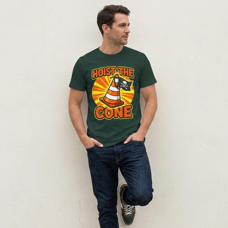 Puede incluir: Camiseta verde oscuro con el texto "HOIST THE CONE" en naranja y blanco, con un cono de tr&aacute;fico de dibujos animados con una bandera pirata. La persona lleva vaqueros azules.