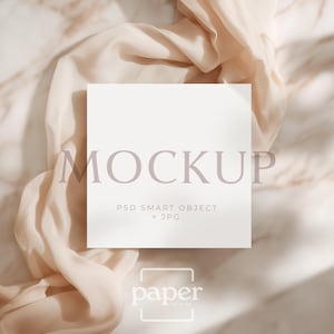Peut inclure: Maquette carrée blanche avec le mot « MOCKUP » dans une police violet clair. La maquette est sur un tissu beige avec un fond en marbre. Le texte « PSD SMART OBJECT + JPG » se trouve sous le mot « MOCKUP ». Le logo « paper is mind » est en bas.