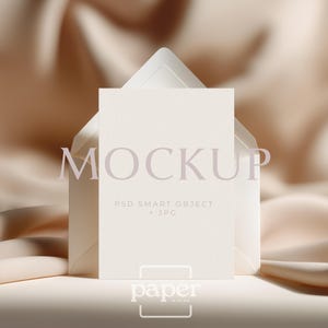 May include: A mockup featuring a cream-colored card inside a matching envelope, set against a backdrop of draped, beige fabric. The word "MOCKUP" is printed across the card, with additional text indicating it's a PSD Smart Object + JPG. The "paper in mind" logo is at the bottom.