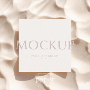 Peut inclure: Une carte carrée blanc cassé avec le mot "MOCKUP" dans une police violet clair. En dessous se trouvent les mots "PSD SMART OBJECT + JPG". La carte est sur une surface beige clair texturée. Le mot "paper" est en bas.