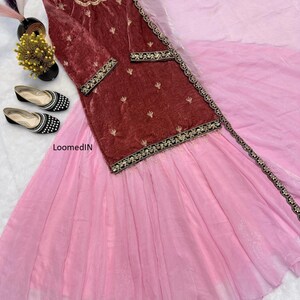 May include: A formal ensemble featuring a maroon velvet top with gold embroidery and a light pink skirt. The top has long sleeves and decorative trim. Black and white embellished flats are placed near the outfit.