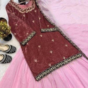 May include: A maroon velvet tunic and skirt set with gold embroidery and a pink dupatta. The tunic has long sleeves and a square neckline. The skirt is a light pink color. The set is displayed on a white surface.