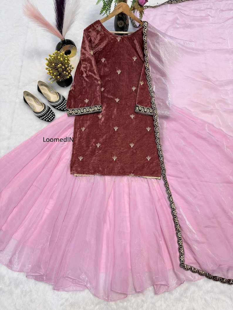 May include: A maroon velvet tunic with gold embroidery and long sleeves is paired with a light pink skirt and a matching sheer scarf. The outfit is displayed with black and white patterned flats and decorative accents.