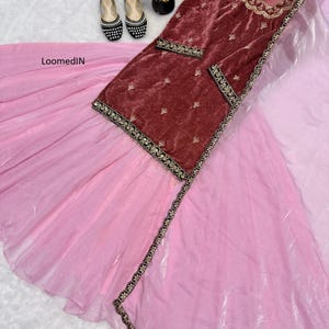 May include: A maroon velvet tunic with gold embroidery and a light pink skirt. The tunic has gold trim and small gold embellishments. Black and white embellished flats are visible. The outfit is displayed on a white surface.