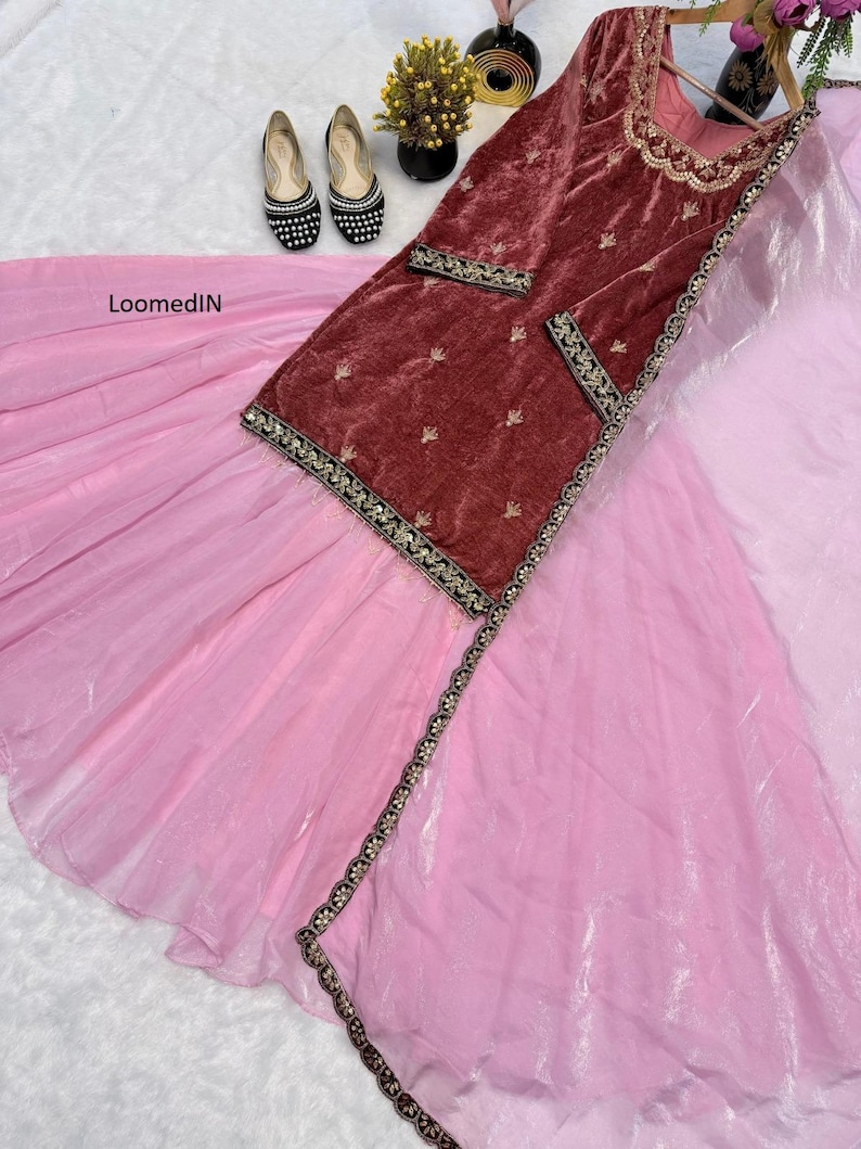 May include: A maroon velvet tunic with gold embroidery and a light pink skirt. The tunic has gold trim and small gold embellishments. Black and white embellished flats are visible. The outfit is displayed on a white surface.