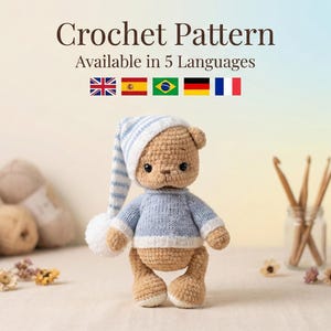 Puede incluir: Un oso de peluche tejido a ganchillo, con un suéter azul y un gorro de dormir a rayas con un pompón blanco. La imagen incluye el texto "Crochet Pattern Available in 5 Languages" con banderas. Hilo y ganchillos en el fondo.