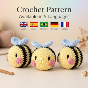 Puede incluir: Tres juguetes de abeja de ganchillo con cuerpos amarillos, rayas negras, alas azules y mejillas rosas. La imagen también muestra ovillos de lana, un ganchillo y el texto "Crochet Pattern Available in 5 Languages" con banderas.