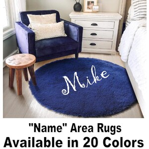 May include: A round, navy blue area rug with the name "Mike" in white script. The rug is in a room with a blue armchair, a small wooden stool, and a white nightstand. Text at the bottom reads "Name" Area Rugs Available in 20 Colors.