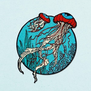 May include: A circular embroidered patch featuring two jellyfish with red caps and blue centers, floating against a bright turquoise background with green seaweed and coral-like structures. The jellyfish have long, thin, dark red tentacles.