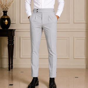 May include: A crisp white long-sleeved button-down shirt paired with light gray high-waisted trousers. The trousers feature a wide waistband with side adjusters, double pleats at the front, and a tapered leg cut with cuffed hems at the ankles.