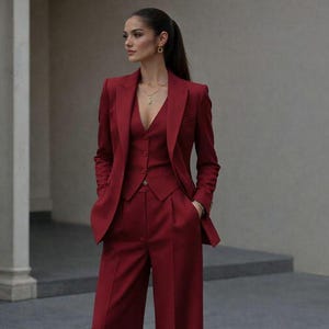 May include: A deep red three-piece suit consisting of a tailored blazer with notched lapels, a button-front vest with a V-neckline, and high-waisted wide-leg trousers with a pressed crease. The ensemble is paired with dark brown pointed-toe heels.