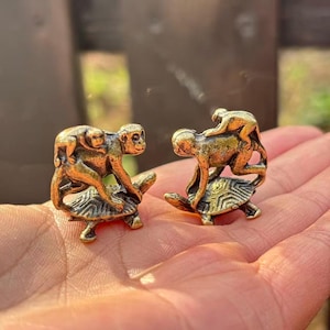 May include: Two small, bronze-colored figurines of monkeys riding turtles. Each monkey figurine has a larger monkey carrying a smaller monkey on its back. The turtles have detailed shell patterns.