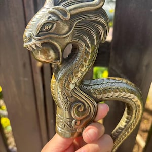 May include: A bronze-colored dragon head cane handle. The handle features intricate details, including scales, horns, and a detailed face. The curved handle is designed for a comfortable grip. The dragon's head is the focal point, showcasing the craftsmanship.