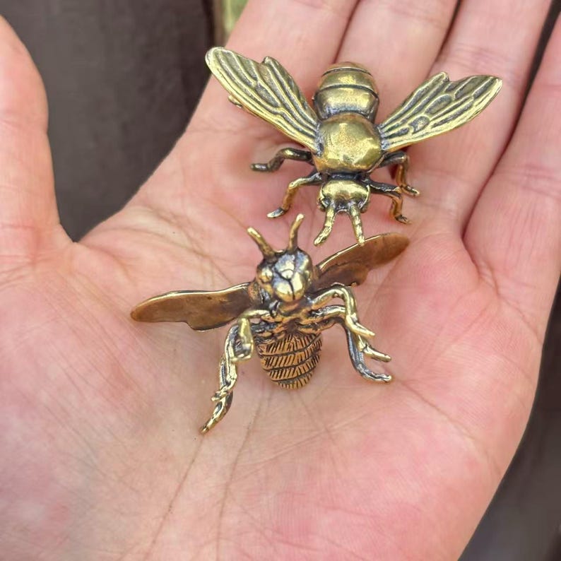 K&ouml;nnte beinhalten: Zwei detaillierte Messing-Bienenfiguren. Die Bienen haben ausgebreitete Fl&uuml;gel und komplizierte K&ouml;rperdetails. Die Figuren befinden sich in einer nat&uuml;rlichen Pose, mit goldenem Farbton, und werden auf neutralem Hintergrund pr&auml;sentiert.