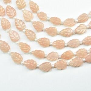May include: A multi-strand necklace featuring pale peach-colored carved leaf-shaped beads alternating with small white round beads. The strands are arranged in a cascading pattern, showcasing the translucent quality of the carved leaf elements.
