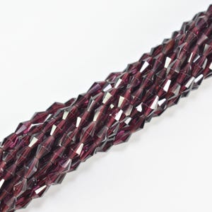 May include: Close-up of strands of dark burgundy faceted beads. The beads are geometric in shape and have a reflective surface, creating a sparkling effect. They are strung together, suitable for jewellery making or crafts.