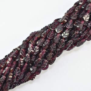 May include: Strands of dark red garnet gemstone beads, carved in a leaf shape. The beads have a polished finish and are strung together, creating a rich, textured appearance. The beads are approximately 0.5 inches in length.