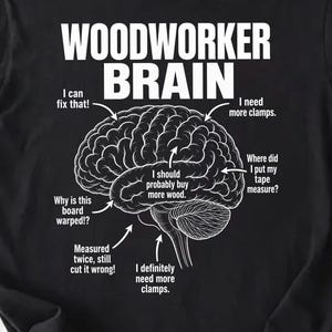 May include: Black t-shirt featuring a white diagram of a brain with woodworking-related thoughts. Text includes "WOODWORKER BRAIN", "I can fix that!", "I need more clamps", and "Why is this board warped?!"