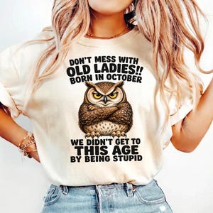 Peut inclure: T-shirt crème avec une illustration détaillée d'un hibou et le texte : "DON'T MESS WITH OLD LADIES!! BORN IN OCTOBER WE DIDN'T GET TO THIS AGE BY BEING STUPID."