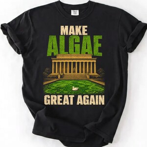 Könnte beinhalten: Ein schwarzes T-Shirt mit einem Grafikdruck des Lincoln Memorials und einem mit grünen Algen bedeckten Reflexionsbecken. Der Text lautet MAKE ALGAE GREAT AGAIN in fetter, abgenutzter Schrift. Eine kleine weiße Ente schwimmt im Becken.