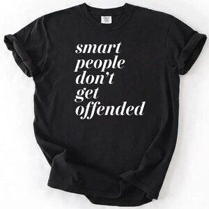 Op de afbeelding: Zwart t-shirt met de witte tekst "smart people don't get offended" in een gestileerd lettertype. Het shirt heeft korte mouwen en een ronde hals. De stof lijkt zacht en comfortabel.