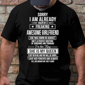 以下が含まれることがあります： 白文字の黒いTシャツ。テキストは「SORRY I AM ALREADY TAKEN BY A FREAKING AWESOME GIRLFRIEND」とその他のフレーズです。シャツのテーマは人間関係と愛情です。