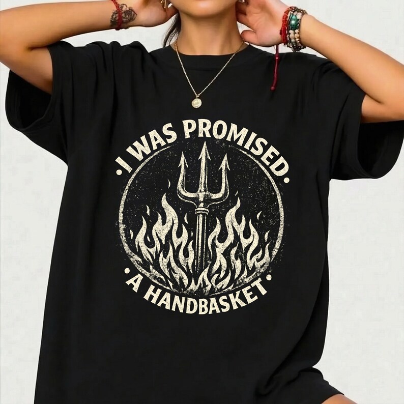 May include: Black t-shirt with a circular graphic. The design features a trident, flames, and the text "I WAS PROMISED. A HANDBASKET." The graphic has a distressed, vintage appearance, with off-white and beige tones.