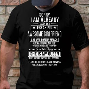 Könnte beinhalten: Schwarzes T-Shirt mit weißem Text. Der Text lautet "SORRY I AM ALREADY TAKEN BY A FREAKING AWESOME GIRLFRIEND" und andere Sätze über eine Freundin. Das Shirt ist ein lässiger Stil.