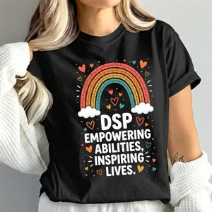 May include: Black t-shirt featuring a colorful rainbow design with the text "DSP Empowering Abilities, Inspiring Lives." The design includes hearts and clouds. The shirt is a crew neck.