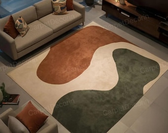 May include: A modern area rug with an abstract design. The rug features a cream-colored background with large, organic shapes in shades of rust and olive green. The rug is placed in a living room setting with a sofa and armchair.