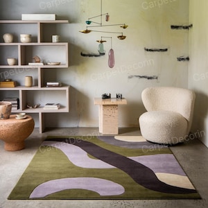May include: A contemporary living room with a green, purple, and brown abstract patterned rug. The room includes a cream-colored chair, a small side table, and a decorative mobile. The walls are painted in a light green colour.