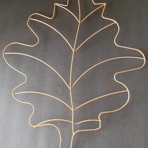 Puede incluir: Escultura decorativa de metal con forma de hoja de roble en color oro claro. La forma de la hoja se crea con finas varillas de metal, formando las venas y el contorno. Diseñada para montaje en pared o como elemento decorativo. Mide unos 30 cm de largo.