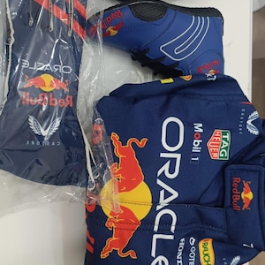 Puede incluir: Un conjunto de equipamiento de Oracle Red Bull Racing que incluye un guante de carreras azul con rayas rojas, una zapatilla de carreras azul con cordones negros y una camiseta de carreras azul oscuro con los logotipos de Oracle, Red Bull, Mobil 1, TAG Heuer y Honda.