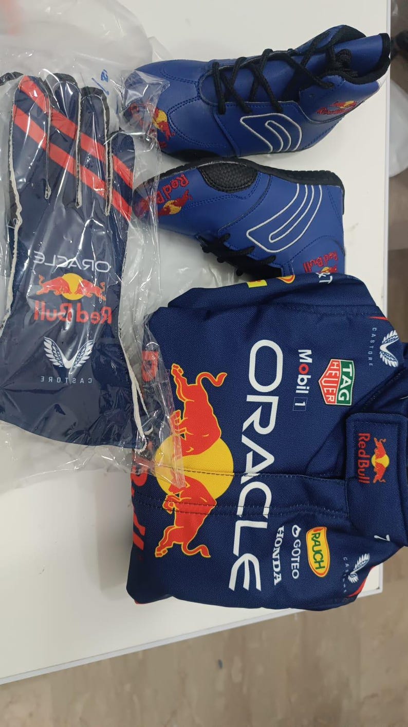 May include: A set of Oracle Red Bull Racing gear including a dark blue long-sleeve shirt with sponsor logos like TAG Heuer, Mobil 1, and Honda, a pair of blue racing gloves with red stripes, and a pair of blue racing shoes with black laces.
