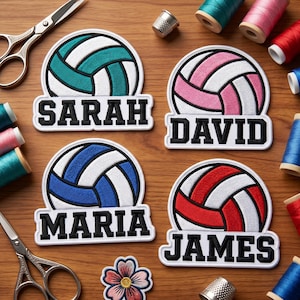 May include: Four personalized volleyball patches in teal, pink, blue, and red, each with a name in black lettering. The patches are surrounded by sewing supplies, including scissors, spools of thread, and thimbles, on a wooden surface.