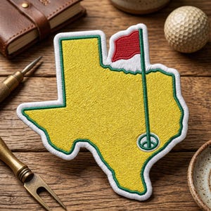 May include: Embroidered patch in the shape of Texas, featuring a golf course design. The patch is yellow with a green border and a red flag on a green pole. A golf ball and other golf accessories are in the background.