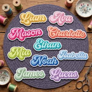 May include: A collection of embroidered name patches in various colors, including yellow, pink, orange, green, blue, and purple. Each patch features a different name in a retro, cursive font with a white border. The patches are arranged on a gray placemat.