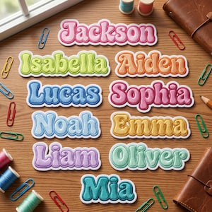May include: Embroidered name patches in various colors, including pink, blue, and green, spelling out names like Jackson, Isabella, and Lucas. The patches have a retro font and are surrounded by a white border. Paper clips and spools of thread are scattered around.