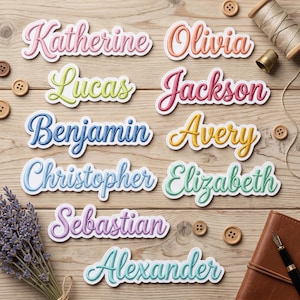 May include: Colorful name stickers in various fonts and colors, including "Katherine," "Olivia," "Lucas," "Jackson," "Benjamin," "Avery," "Christopher," "Elizabeth," "Sebastian," and "Alexander." The stickers are arranged on a wooden surface with sewing notions and a pen.